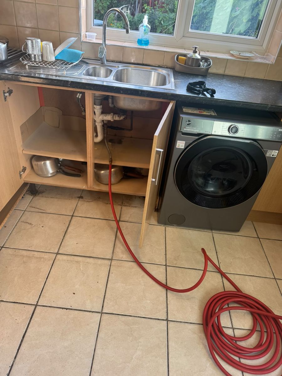 Red hose connected to the pipework under a kitchen sink, ready for tracer gas leak detection